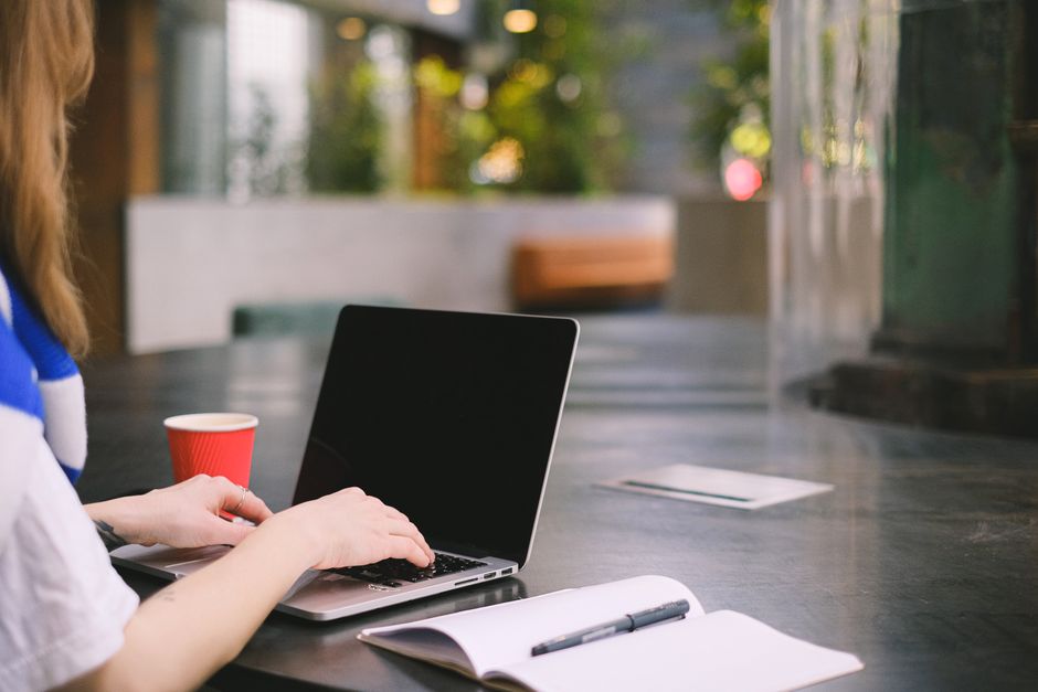 Person typing on a laptop in a modern indoor workspace with coffee and notebook.